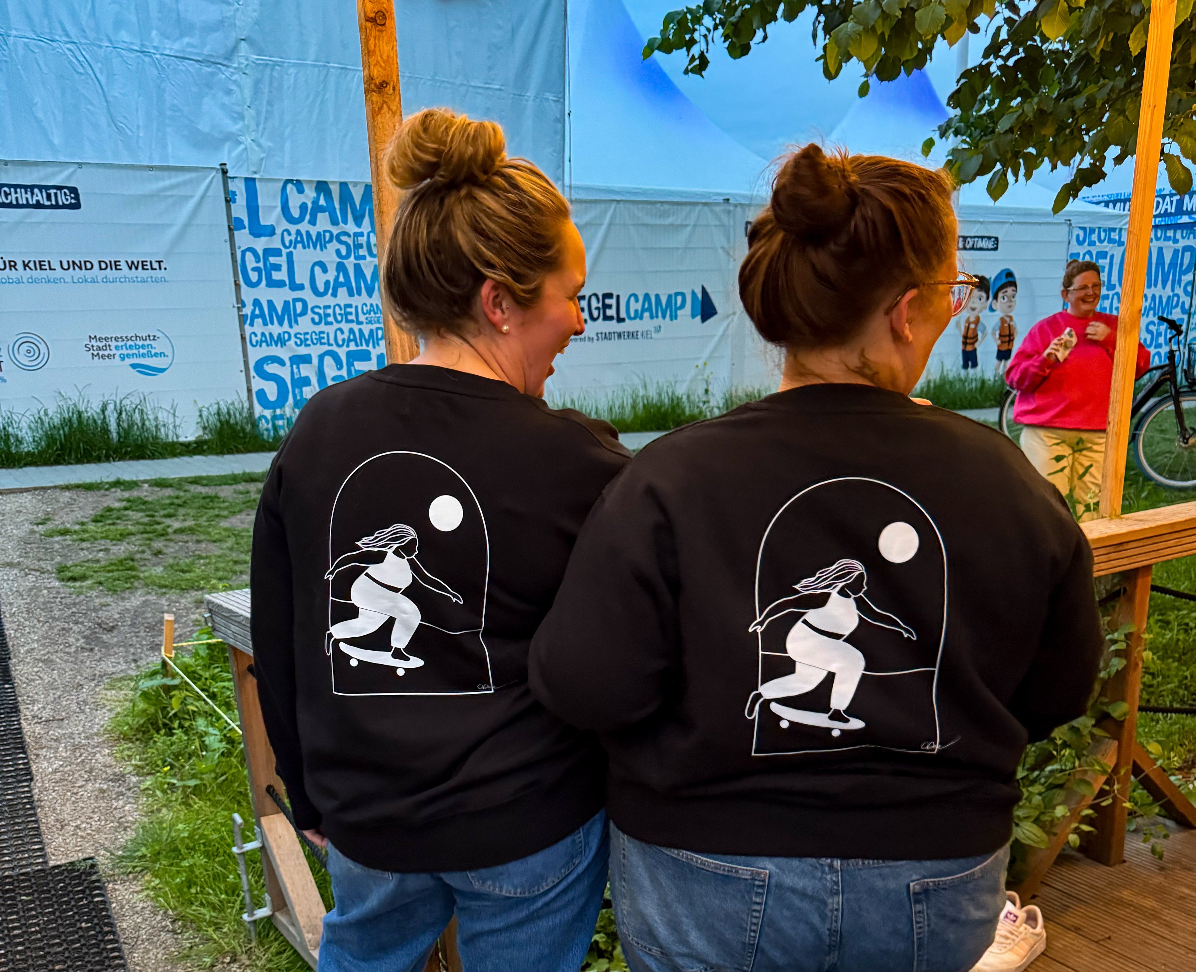 Zwei Mädels tragen das Sweatshirt Sweta von CURVYBEACHGIRL mit dem "Curvy Skatergirl"-Druck auf dem Rücken